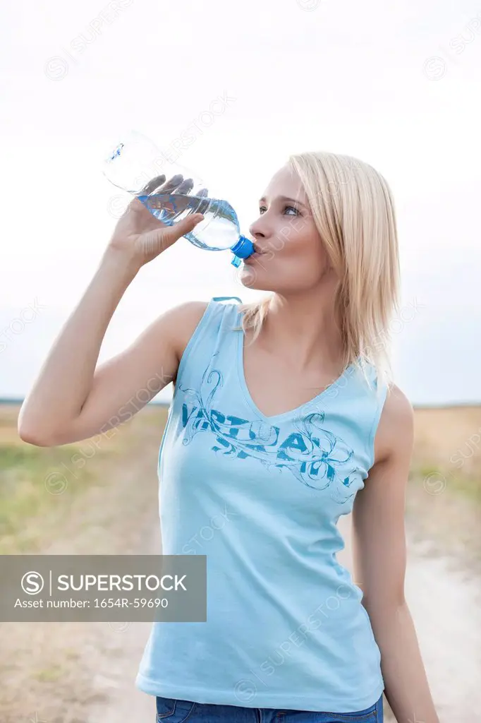 Young woman drinking water from bottle on field