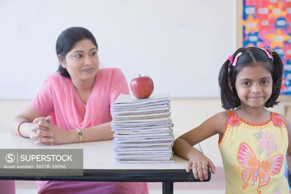 Portrait of a schoolgirl smirking with a teacher sitting at a desk behind her