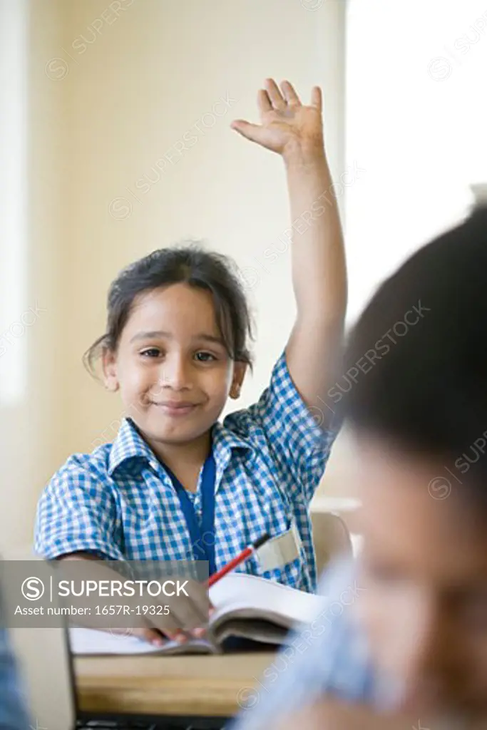 Portrait of a schoolgirl sitting in a classroom with her hand raised