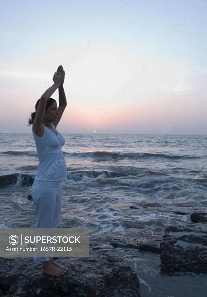 Side profile of a young woman meditating in a prayer position on the beach, Mud Island, Mumbai, Maharashtra, India