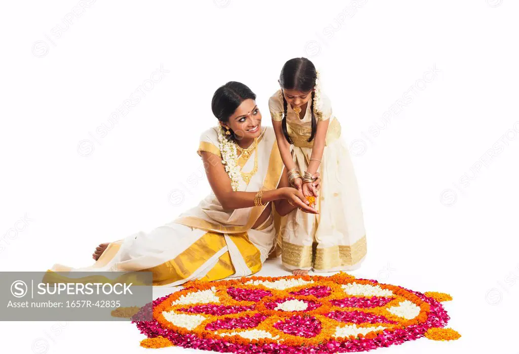 South Indian woman making a rangoli of flowers with her daughter at Onam