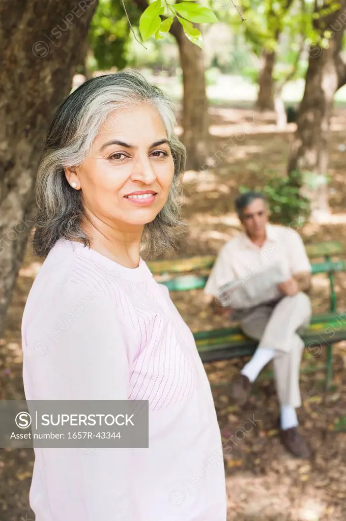 Woman leaning against a tree with her husband reading a newspaper in the background, Lodi Gardens, New Delhi, India