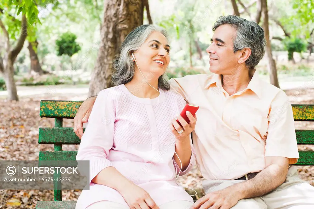 Mature couple listening to music with an MP3 player and smiling, Lodi Gardens, New Delhi, India