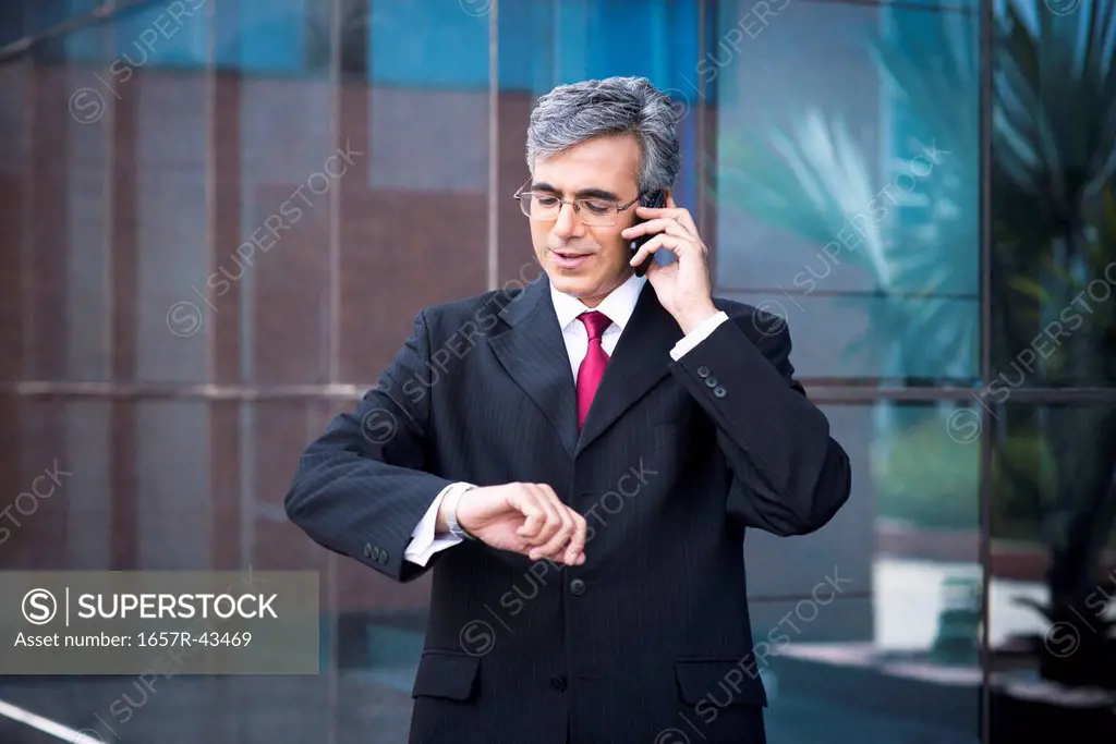 Businessman talking on a mobile phone and looking at his wristwatch