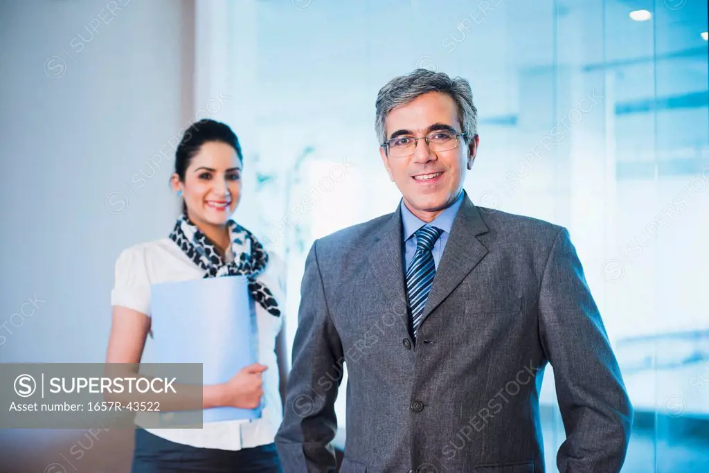 Businessman smiling with his secretary standing behind him