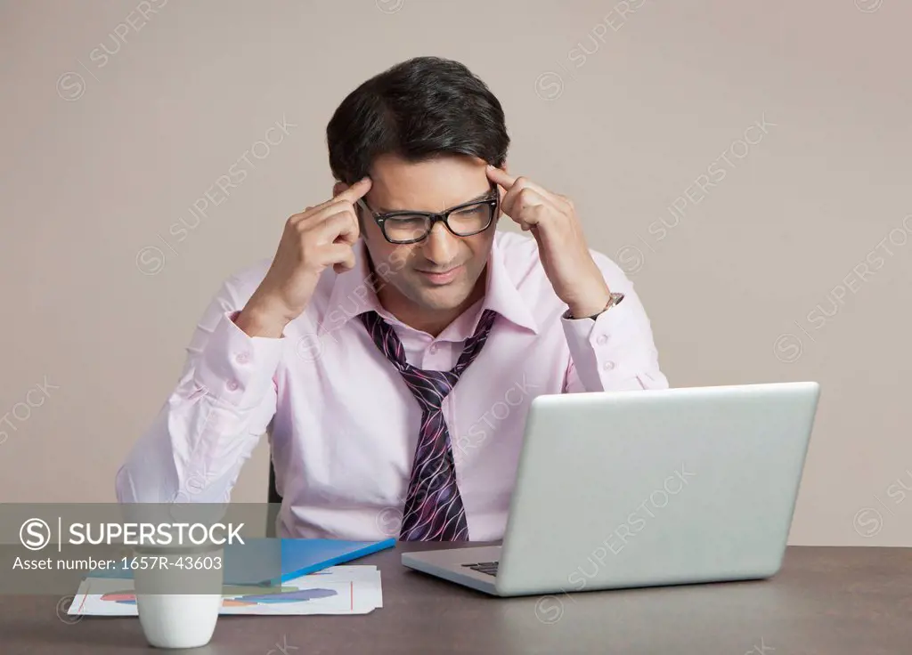 Businessman suffering from headache and looking at a laptop