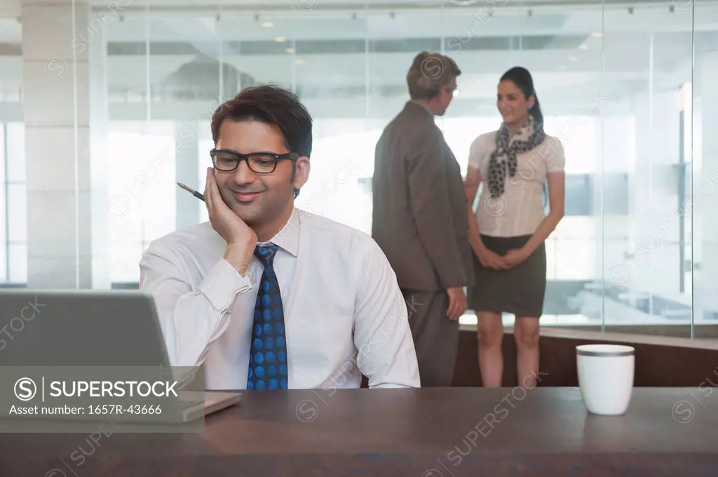 Businessman looking at a laptop with their colleagues standing in the background