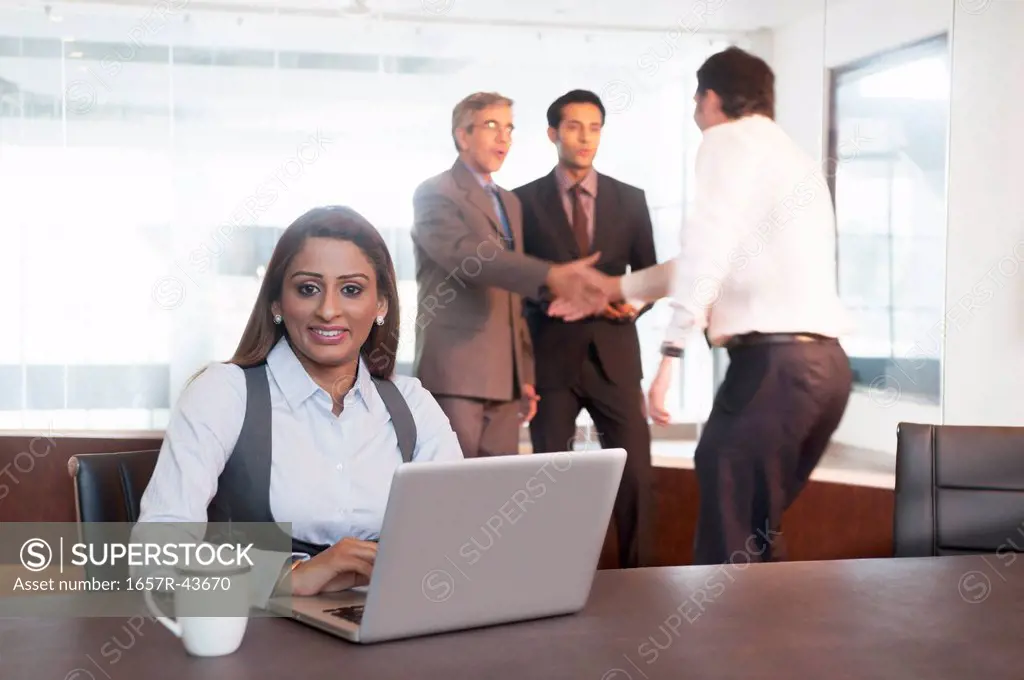 Businesswoman using a laptop with their colleagues standing in the background