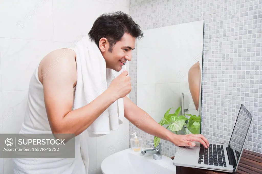 Man using a laptop while brushing his teeth