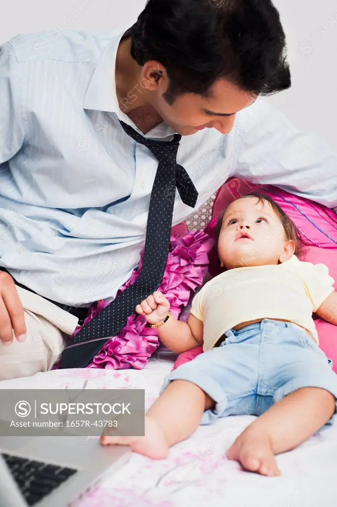Businessman using a laptop and looking at his baby on the bed