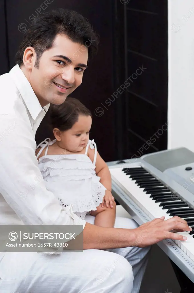 Man playing electronic piano with his daughter sitting on lap