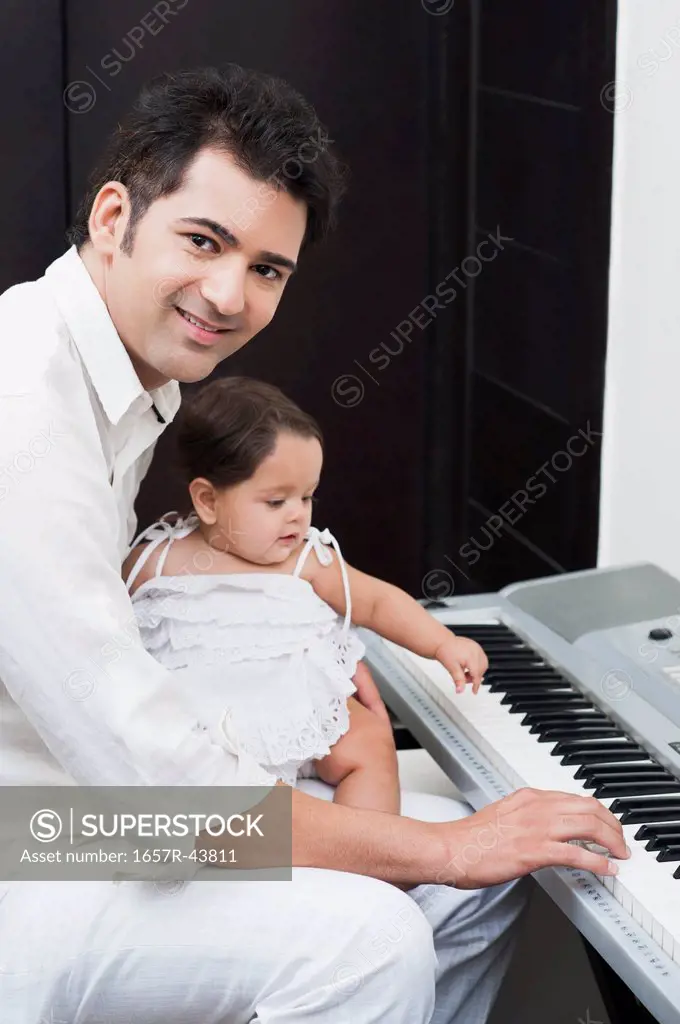 Man playing electronic piano with his daughter sitting on lap