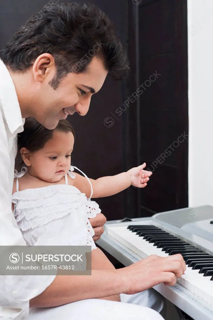 Man playing electronic piano with his daughter sitting on lap