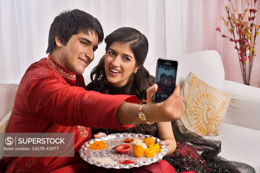 Brother and sister taking a picture of themselves with a mobile phone at Raksha Bandhan
