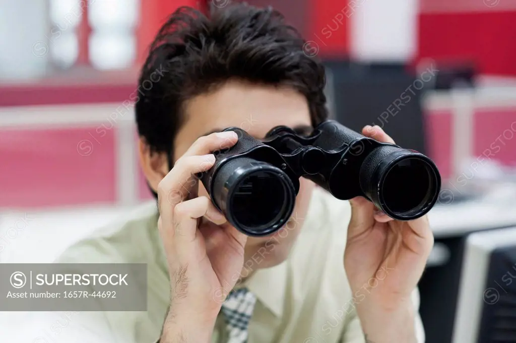 Businessman looking through binoculars in office