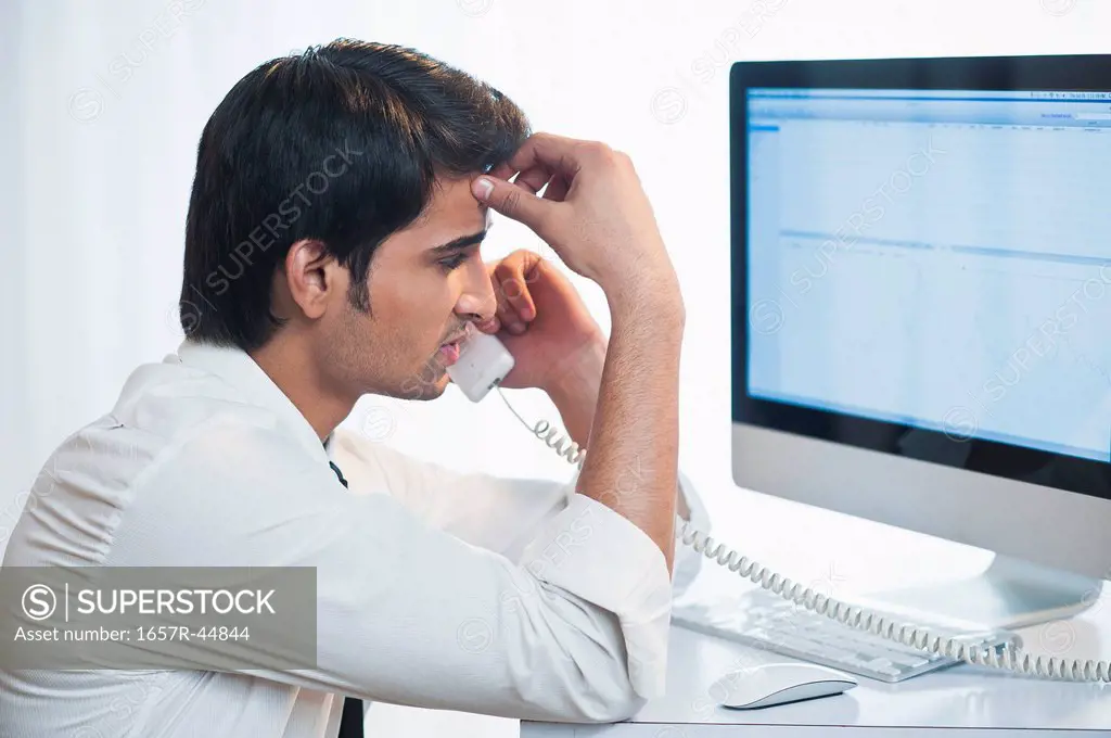 Businessman looking at a computer while talking on a landline phone