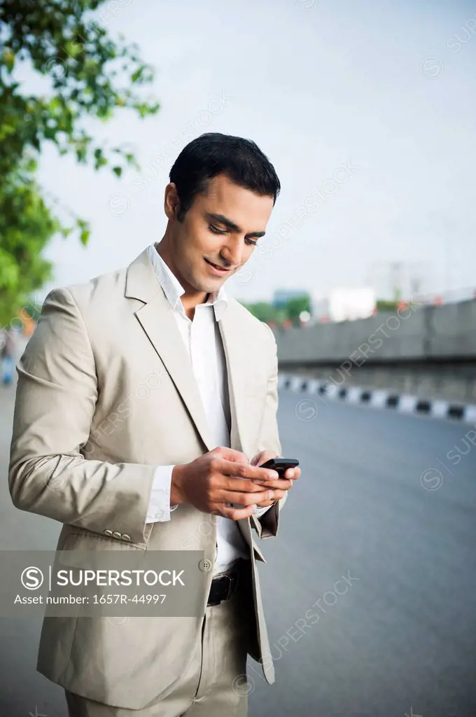 Businessman text messaging on a mobile phone at roadside