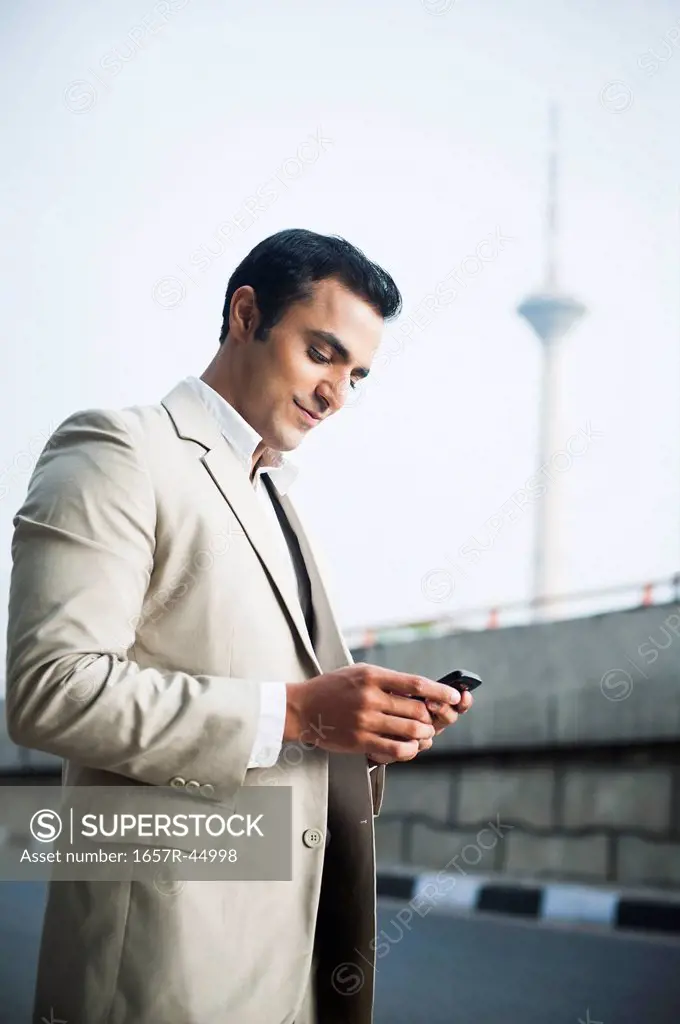 Businessman text messaging on a mobile phone at roadside
