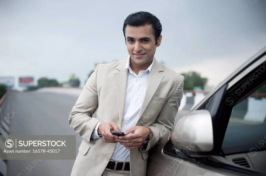 Businessman text messaging on a mobile phone and smiling at a flyover