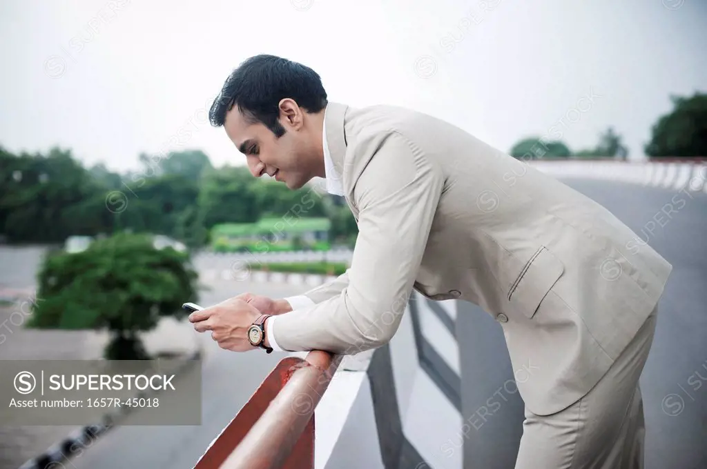 Businessman text messaging on a mobile phone at a flyover