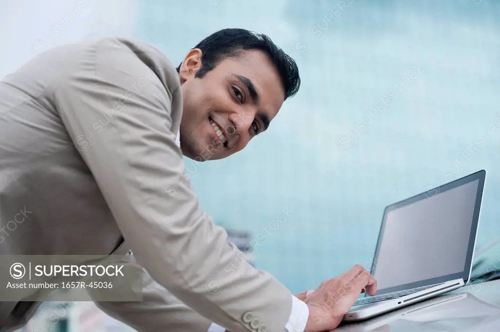 Portrait of a businessman using a laptop on car bonnet and smiling