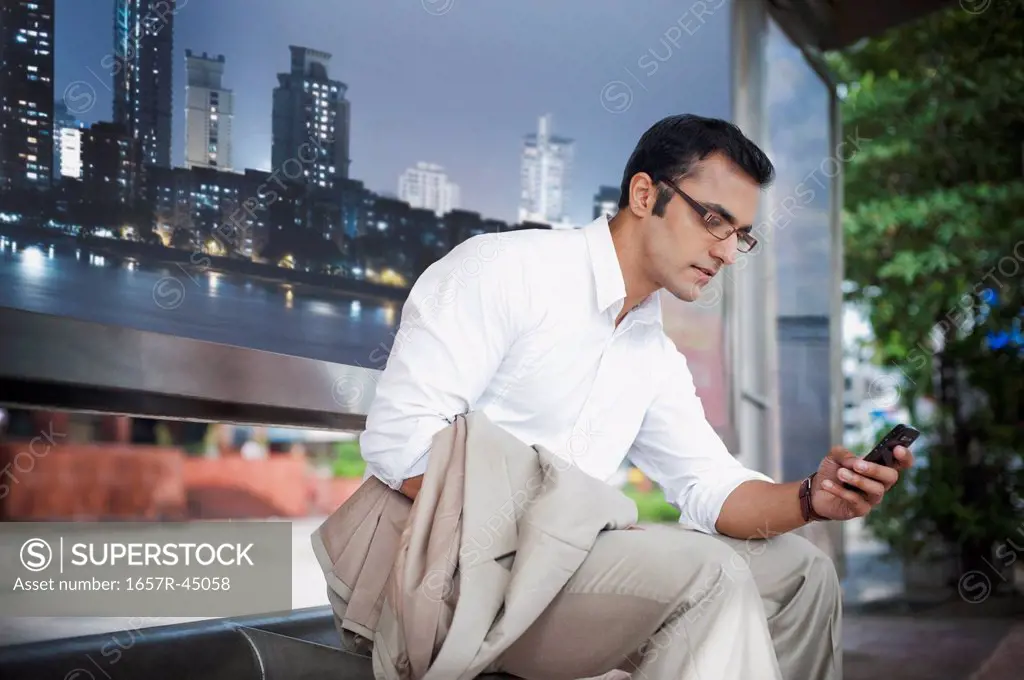 Businessman text messaging on a mobile phone at bus stop