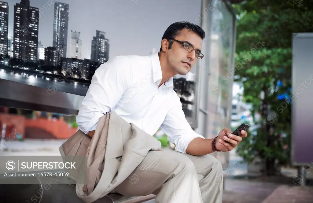 Businessman text messaging on a mobile phone at bus stop