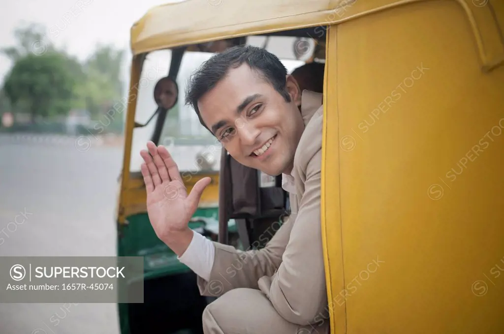 Businessman waving while traveling in an auto rickshaw