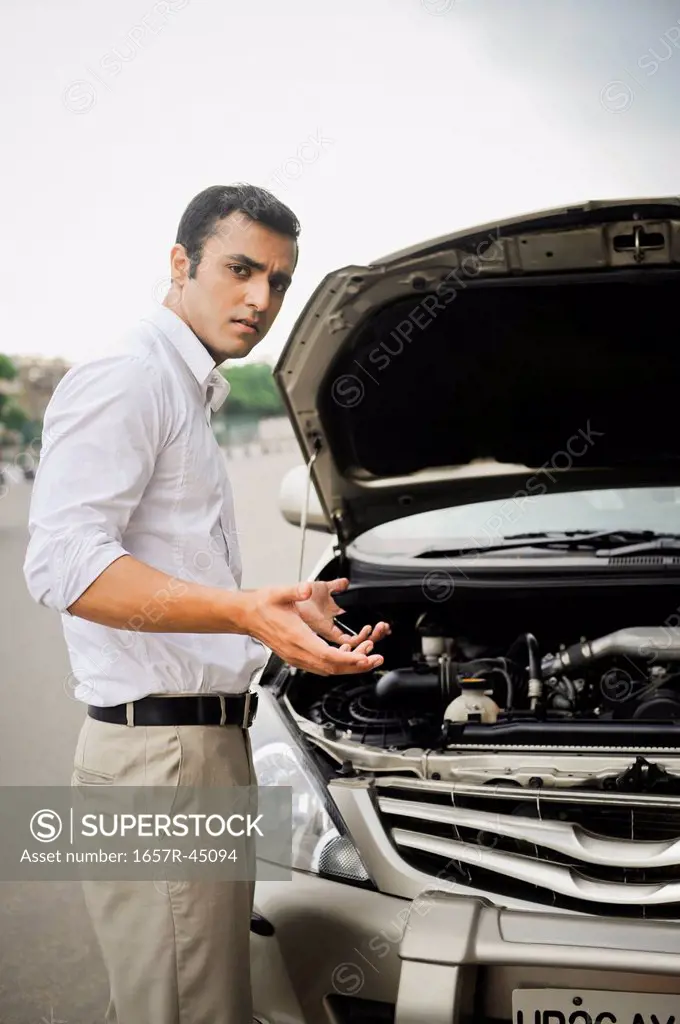 Worried businessman standing beside a breakdown car
