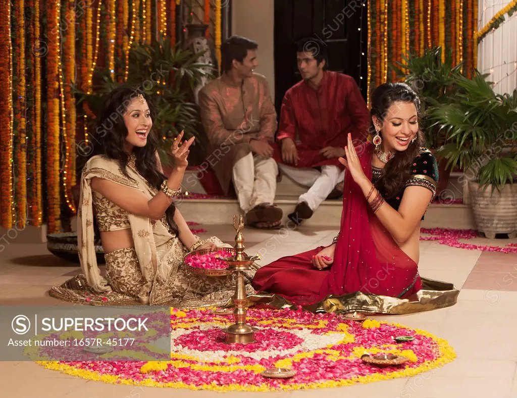 Female friends playing with flowers with male friends sitting in the background on Diwali