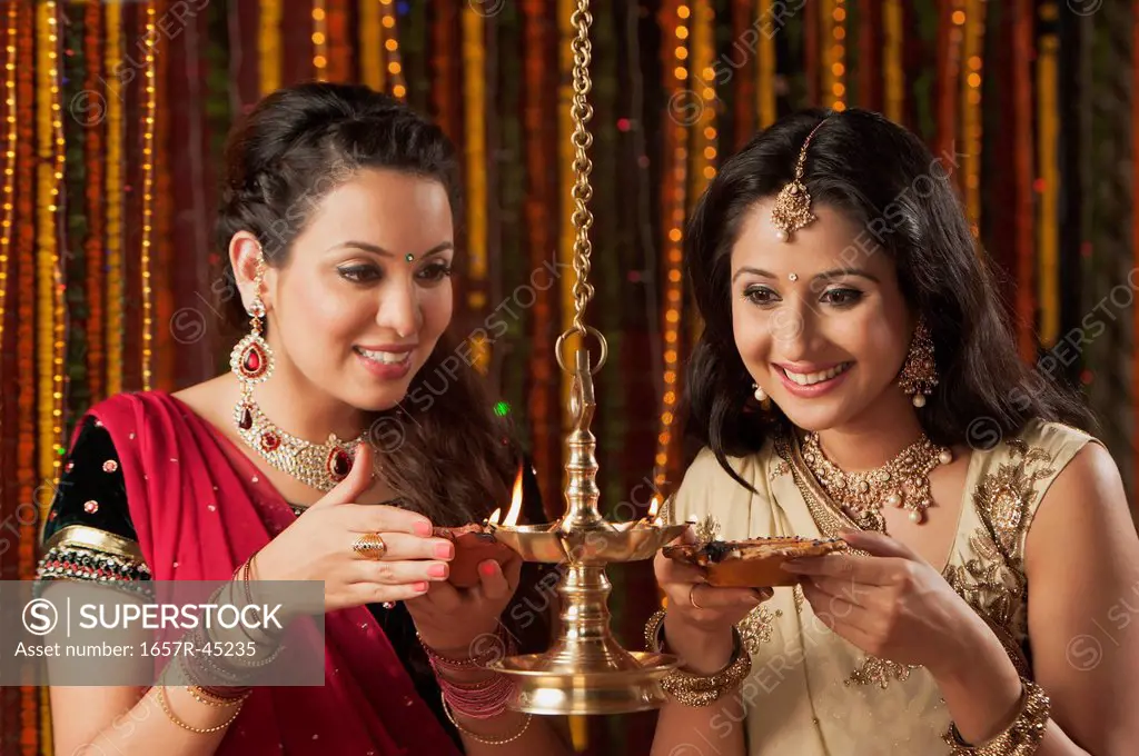 Female friends burning oil lamps on Diwali