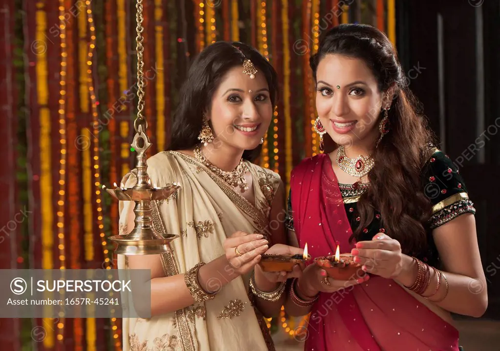 Female friends holding oil lamps on Diwali