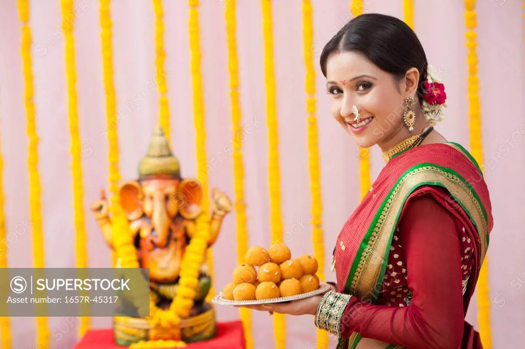 Maharashtrian woman holding laddu in a plate during ganesh chaturthi festival