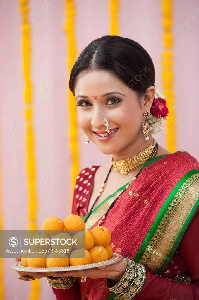 Maharashtrian woman holding laddu in a plate and smiling during ganesh chaturthi festival