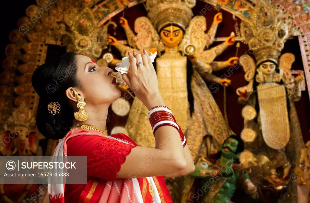 Woman in Bengali sari blowing conch shell