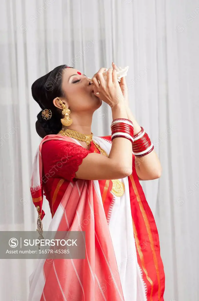 Woman in Bengali sari blowing conch shell