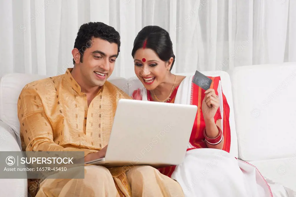 Bengali couple doing online shopping with a credit card and smiling