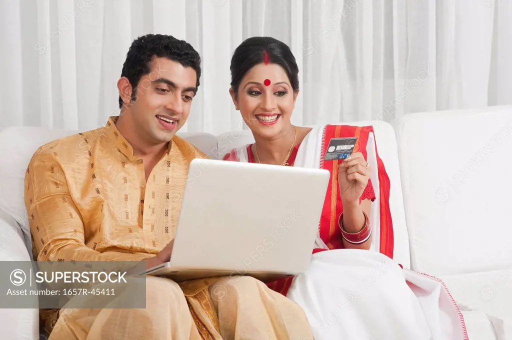 Bengali couple doing online shopping with a credit card and smiling