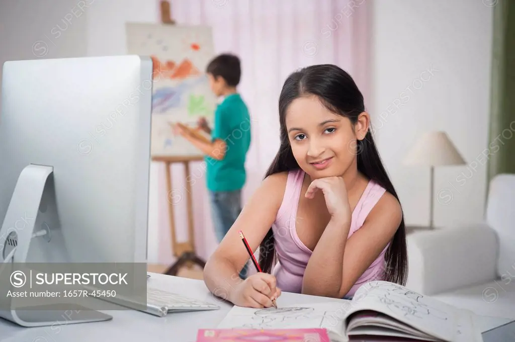 Girl studying at a study table with her brother painting on artist's canvas