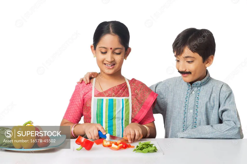 Boy imitating like husband standing beside a girl imitating like his wife cutting vegetables