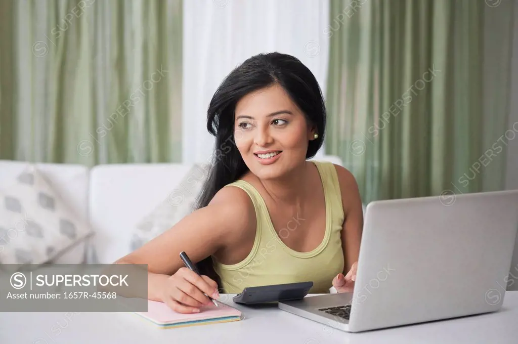 Woman sitting in front of a laptop and writing in a diary