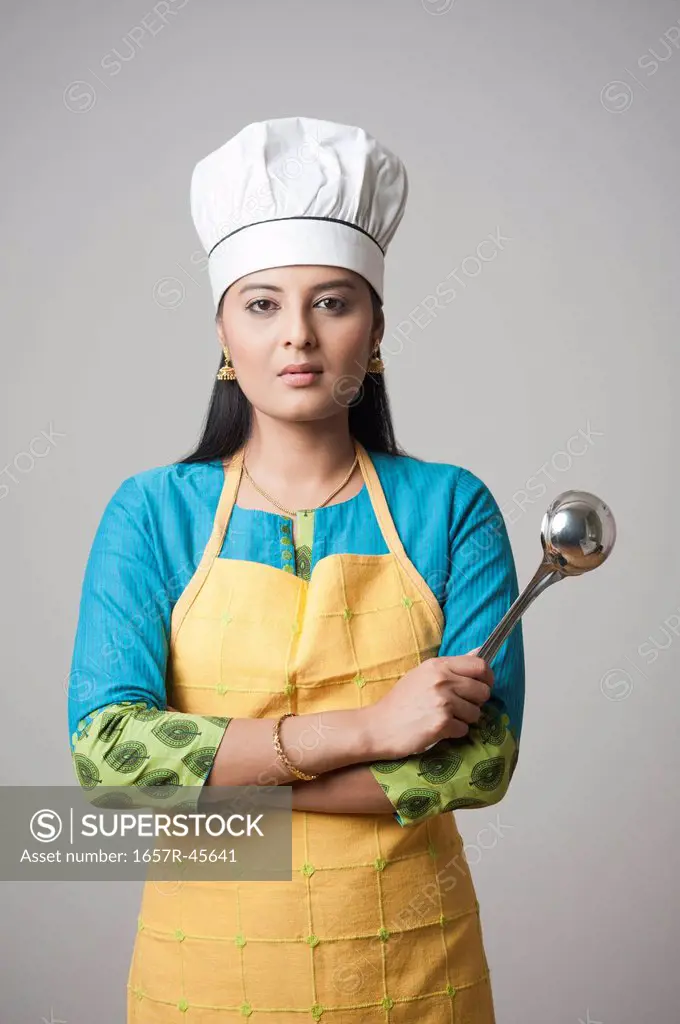 Woman wearing a chef's hat standing with his arms crossed holding a ladle
