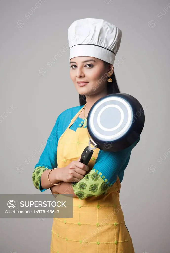 Woman wearing a chef's hat standing with his arms crossed holding a frying pan