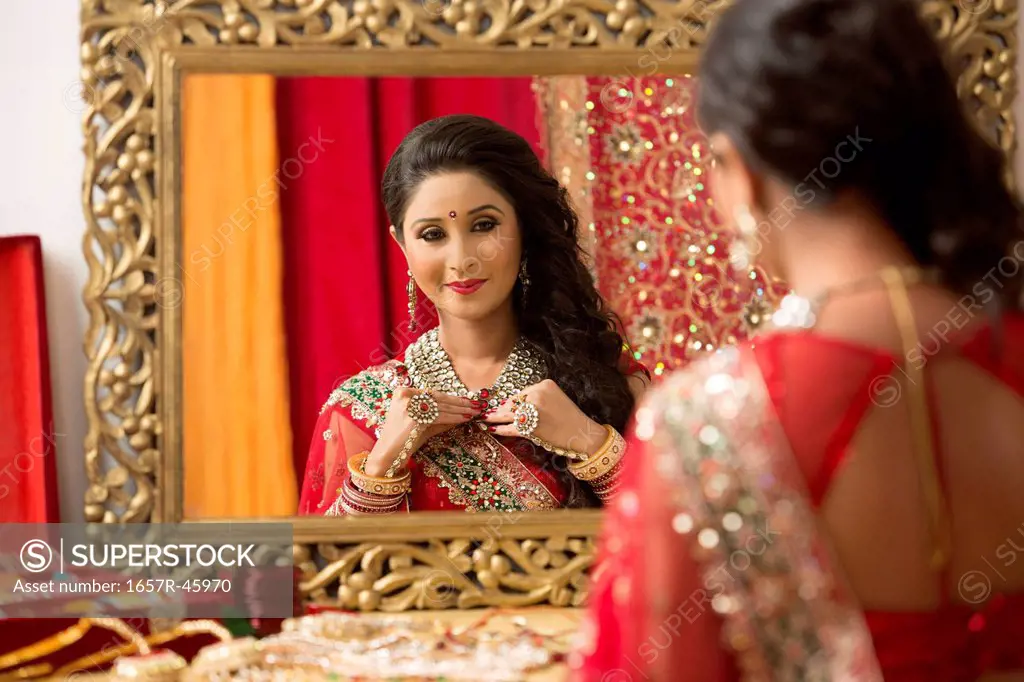Reflection of a bridal woman in mirror putting on necklace