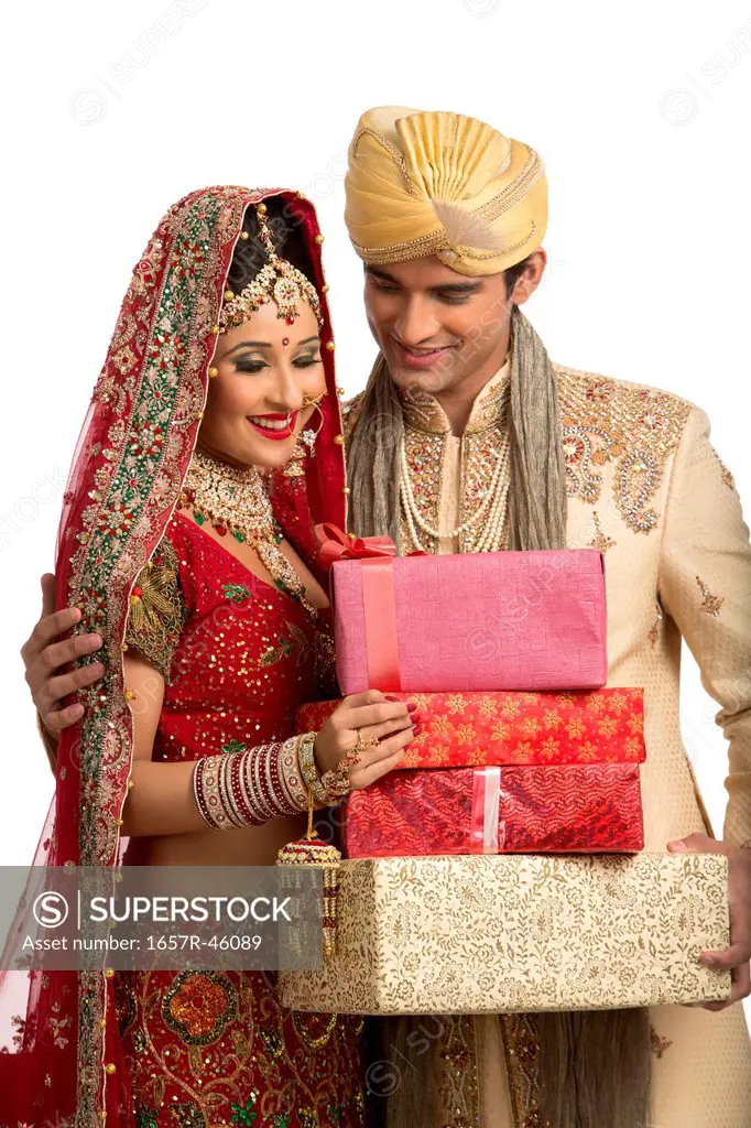 Indian newlywed couple in traditional wedding dress holding gifts