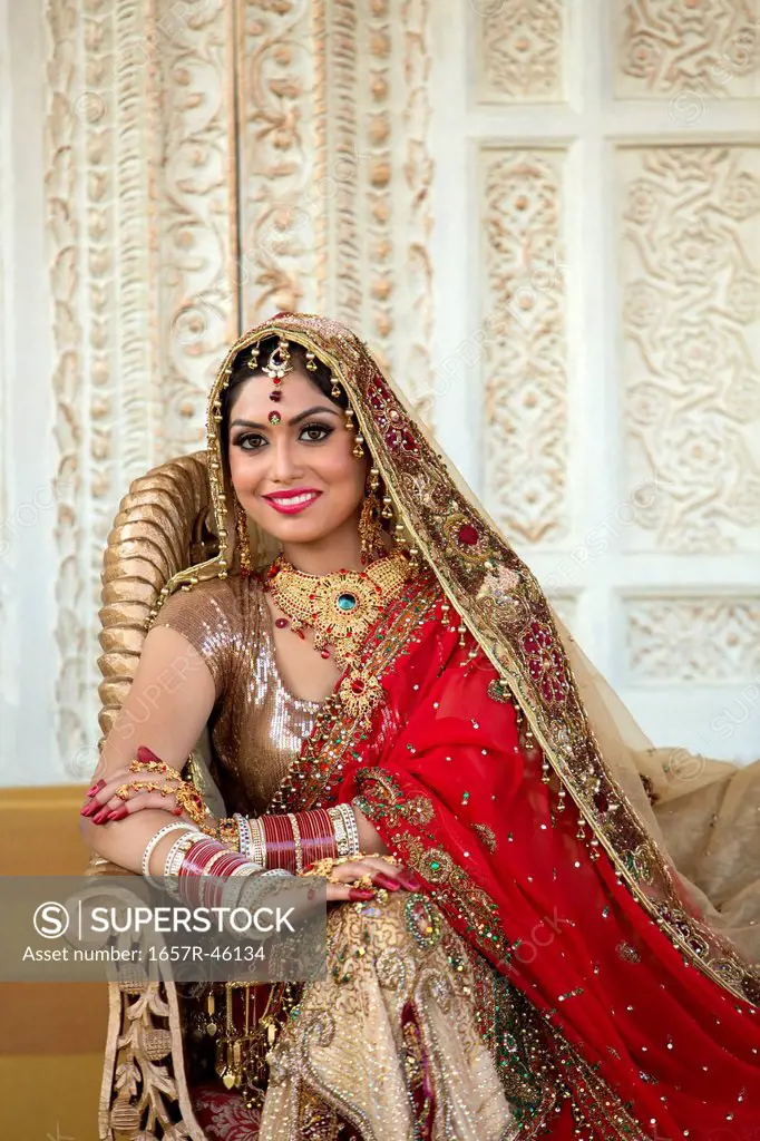 Indian bride in traditional wedding dress sitting on a couch