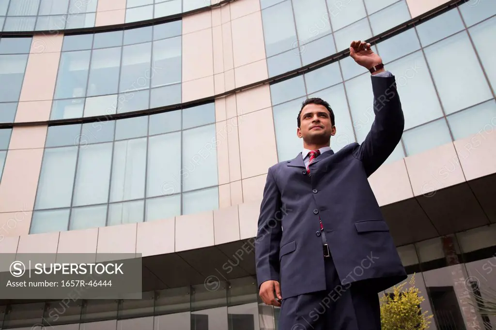 Businessman standing outside an office building with his hand raised