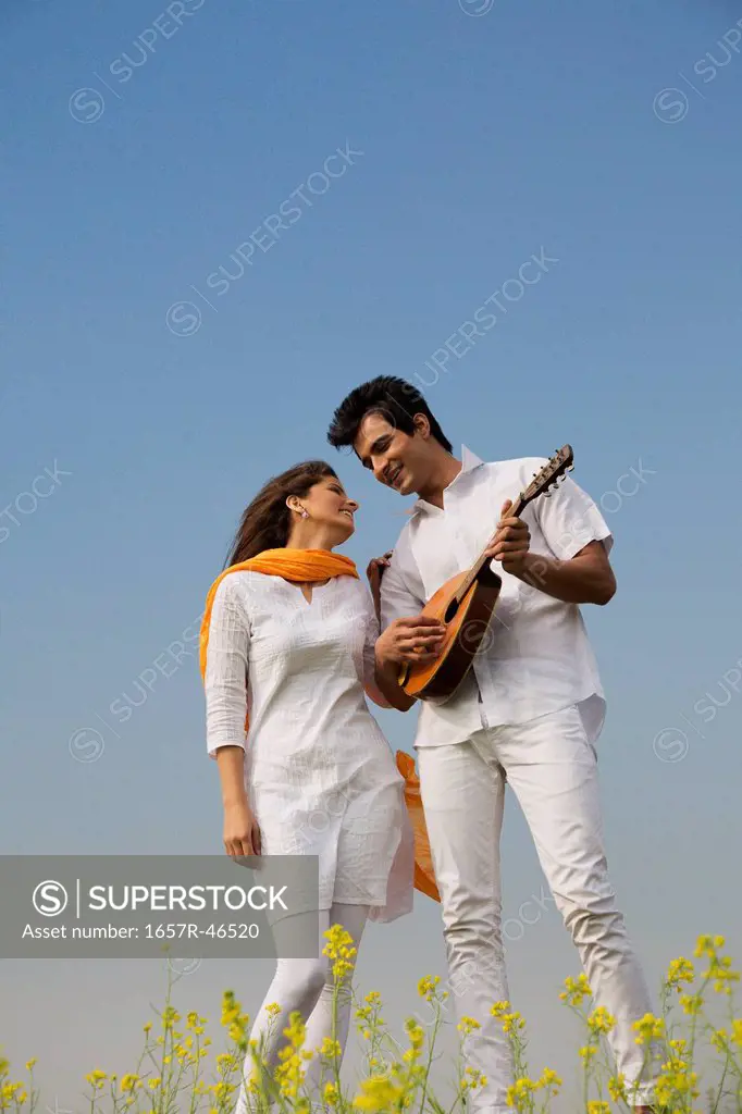 Couple standing in a mustard field with a mandolin