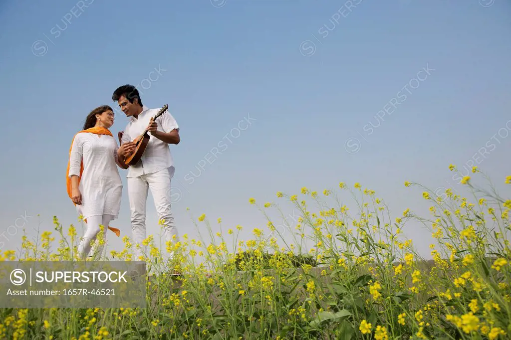 Couple standing in a mustard field with a mandolin