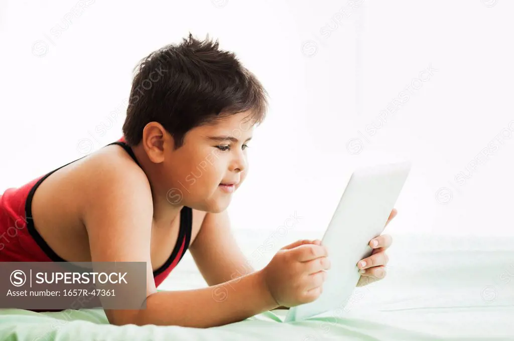 Boy lying on the bed and using a digital tablet